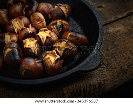 Heap of grilled edible chestnuts in cast iron skillet over dark wooden surface with textile napkin Royalty-Free Stock Photo #345396587