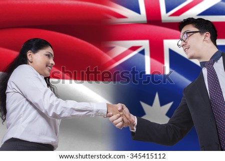 Photo of a young Australian businessman shaking hands with Indonesian woman in front of Australian and Indonesian flags