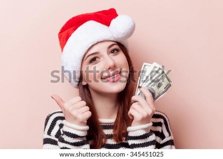 Portrait of a young redhead woman in Santa Claus hat with money on pink background