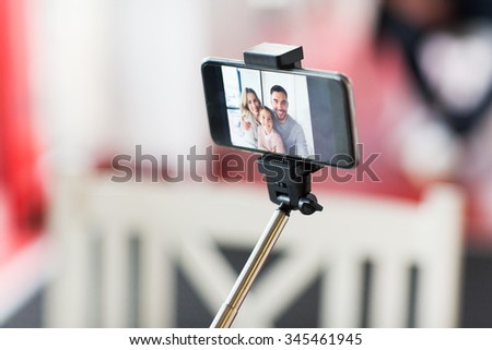 technology and people concept - close up of happy family picture on smartphone screen with selfie stick