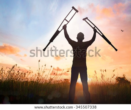 International Day of Persons with Disabilities (IDPD) concept: Silhouette a disabled man standing up and raising his crutches at meadow autumn sunset background Royalty-Free Stock Photo #345507338