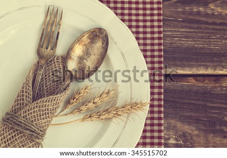 Vintage toned picture of the fork and spoon with the ears of wheat on the old dish at wooden background. Top view.
