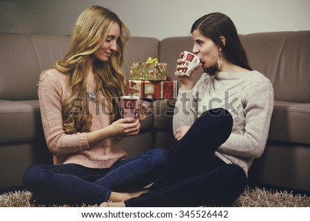 Two women drink from christmas cups on holiday. Color effects and custom white balance are used on this picture.