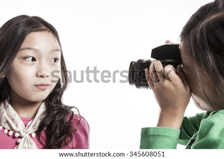 A girls(kid, student, woman, female) wearing pink and green shirts hold a camera with friend with smile isolated white.