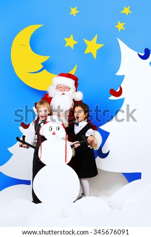 Santa Claus standing with happy children in a cartoon fairy snowy forest. Full length portrait.