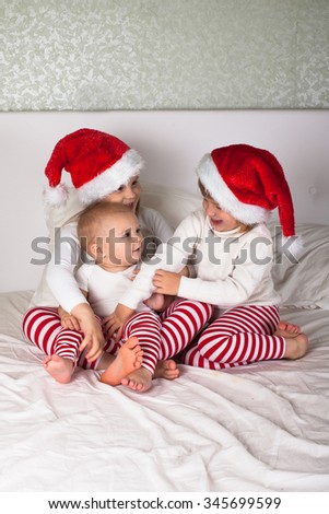 funny kids in their pajamas and Christmas caps on the bed, Christmas and New Year concept, with gifts