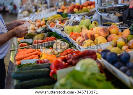 Picture of grocery stall with various fresh fruits and vegetables and man making purchases. 