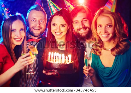 Joyful friends with birthday cake cheering in night club