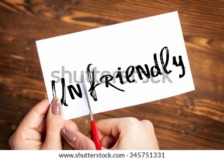 Woman hands cutting card with the word unfriendly 