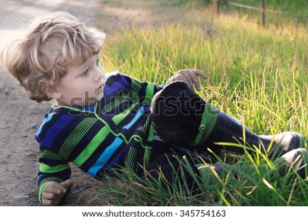 Shot of 3 year old boy lying down in the grass next to a farm road