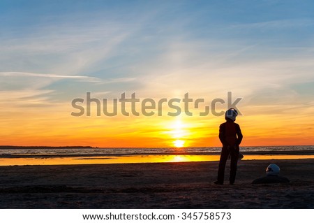 Woman biker silhouette standing on multicolored sunset on the beach. Vibrant blue sky background. Summertime outdoors horizontal image.