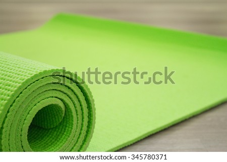 Green yoga mat unrolled on the wooden floor.	
