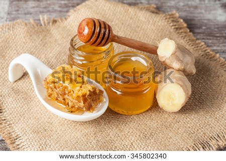 Honey dripping from a wooden honey dipper in a jar on wooden grey rustic background. Ginger and cinnamon.