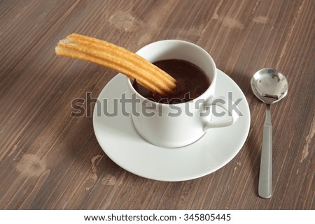 cup of liquid chocolate and churros on a wooden table