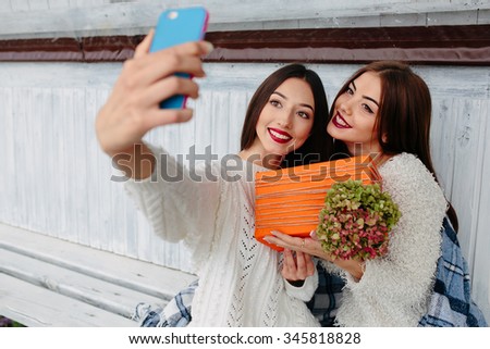 Two girls sit on a bench outside and make selfie with gift