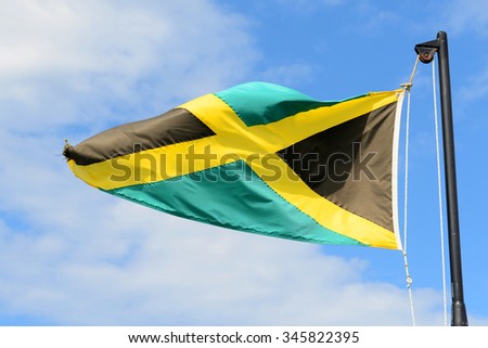 Flag of Jamaica waving against blue sky. Flag of Jamaica have a gold saltire on a green and black field.