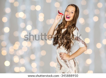 people, style, holidays, celebration and fashion concept - happy young woman or teen girl in fancy dress with sequins and party horn over holidays lights background