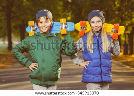 Smiling boy and girl holding color plastic penny boards or skateboards outdoor