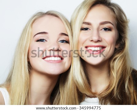Two young girl friends standing together and having fun. Looking at camera.