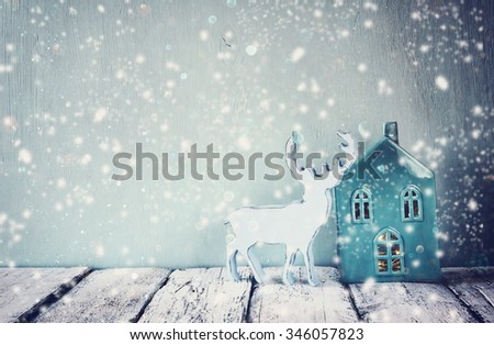 low key photo of vintage aqua porcelain house and reindeer on wooden table. retro filtered image with glitter and snow overlay
