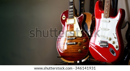 Electric guitars resting on a guitar stand in a darkish room or studio, with plenty of copy space.Shallow depth of field.   Royalty-Free Stock Photo #346141931