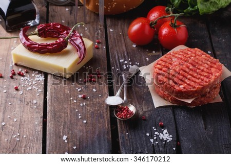 Raw Ground beef meat Burger steak cutlets with seasoning, cheese, tomatoes, salad and bun on vintage wooden boards, black background