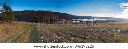 Panoramic landscape of fields at late autumn or winter with little snow and withered trees and grassland. Polish landscape