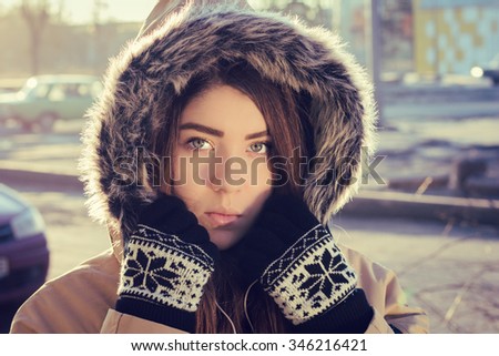 Portrait close up  of a teenage girl outdoor wearing gloves and winter coat with the faux - fur hood on. Toned effect