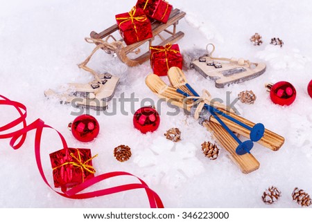 Xmas or new year composition with holiday decorations - little cristmas baubles, red satin ribbon on snow with toy skates, skis and gifts on the sledge. Christmas card
