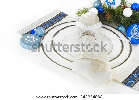 Place setting using white china dishes with black and gold trim topped with a sparkly napkin in a silver ring tied with a white bow. Evergreen and blue and white decorations for Hanukkah. Copyspace