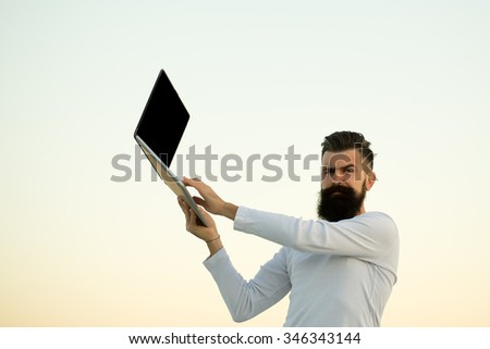 One handsome young bearded business man in white sweater holding and working on laptop outdoor on light sky natural background, horizontal picture
