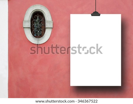 Single hanged empty paper sheet frame with clip on red plastered wall background with small oval historical window nearby
