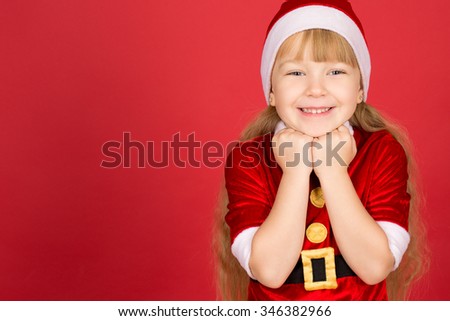 Christmas fever. Horizontal portrait of a little adorable girl in Christmas outfit posing in studio against red background 