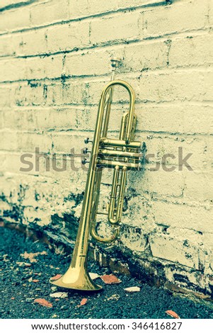 Old worn trumpet stands alone against a grungy pealing white brick wall outside a jazz club