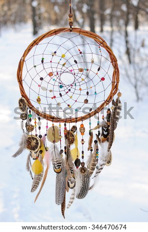 Handmade colorful dream catcher in the snowy forest. Tribal elements, owl feathers