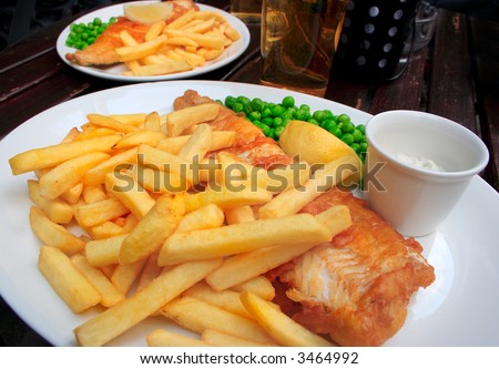 Two plates with fish, chips, peas and sauce on a table.