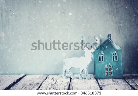 low key photo of vintage aqua porcelain house and reindeer on wooden table. retro filtered image with glitter overlay
