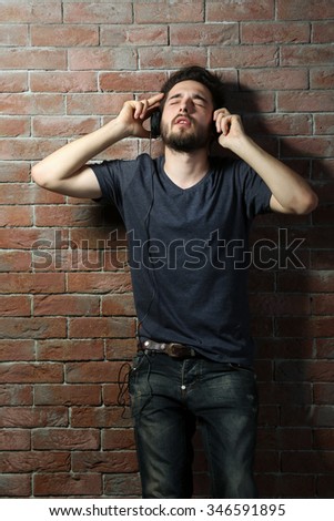 Young handsome man listening music with headphones on brick wall background