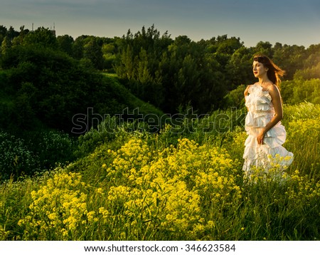 Russian girl in a white dress in a field with hills and yellow flowers