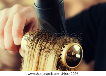Drying blond hair with hair dryer and round brush.  Royalty-Free Stock Photo #346642229