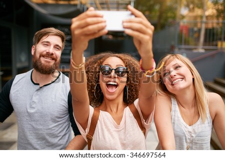 Group of smiling friends taking selfie with mobile phone. Multiracial man and women enjoying themselves outdoors and taking pictures with smart phone.