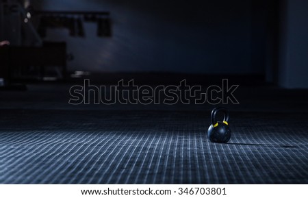 Close up wide angle view of a kettle bell weight on the floor of a gym with moody light.