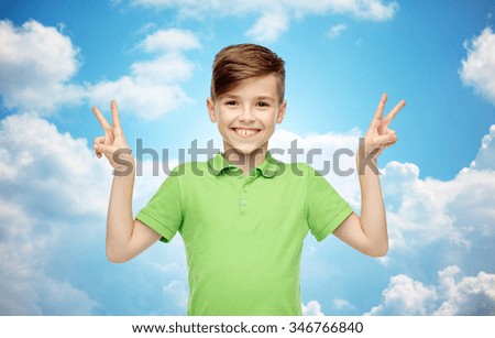 gesture, triumph, childhood, fashion and people concept - happy smiling boy in green polo t-shirt showing peace or victory hand sign over blue sky and clouds background