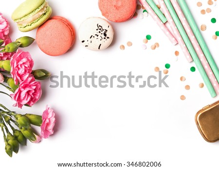 Macarons, paper straws in pastel color, pink flowers and confetti on the white background, top view