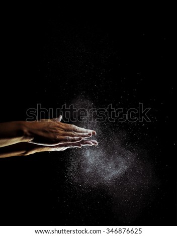 A woman beats her hands together, and white flour fly through the air. The shutter speed has been very fast. Image includes a effect.