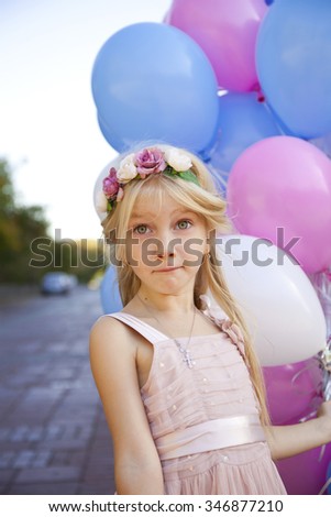 Little five-year girl in a pink dress holding balloons, against background of summer street