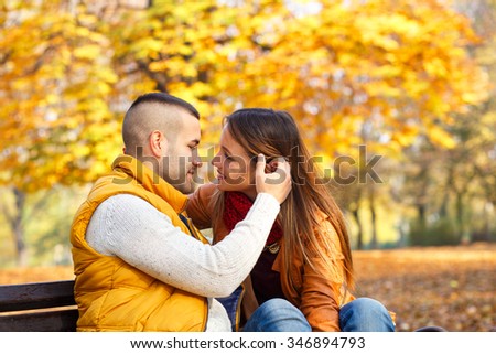 Young couple sitting on a park bench on a sunny autumn day and expressing tenderness