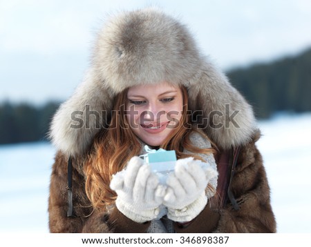 happy young redhair girl  with gift and snow in  hands. Christmas and winter shopping concept, forest in background