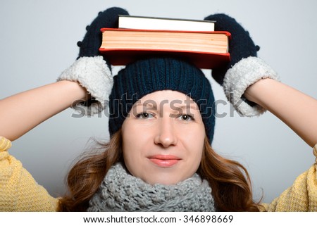 Beautiful girl holding a book on her head, bright in yellow, lifestyle winter clothes studio photo isolated on a gray background