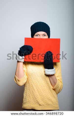 Beautiful girl hiding behind the book, in bright yellow, lifestyle winter clothes studio photo isolated on a gray background